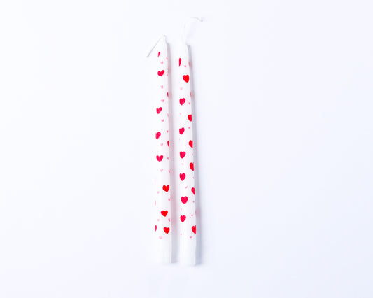 Two white candles with red heart patterns on a white background